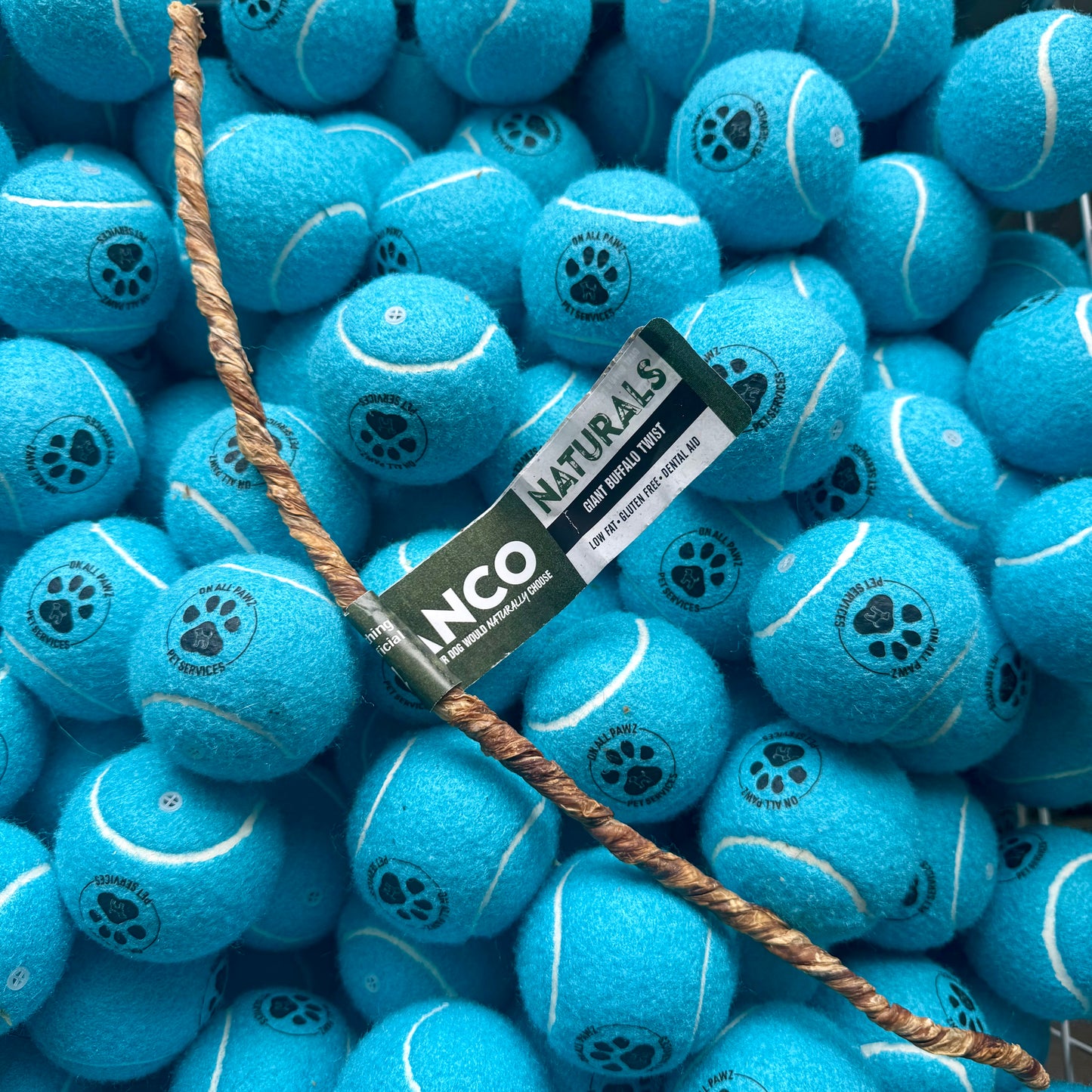 Blue tennis balls with paw prints and a NCO Naturals label, surrounded by more blue tennis balls.