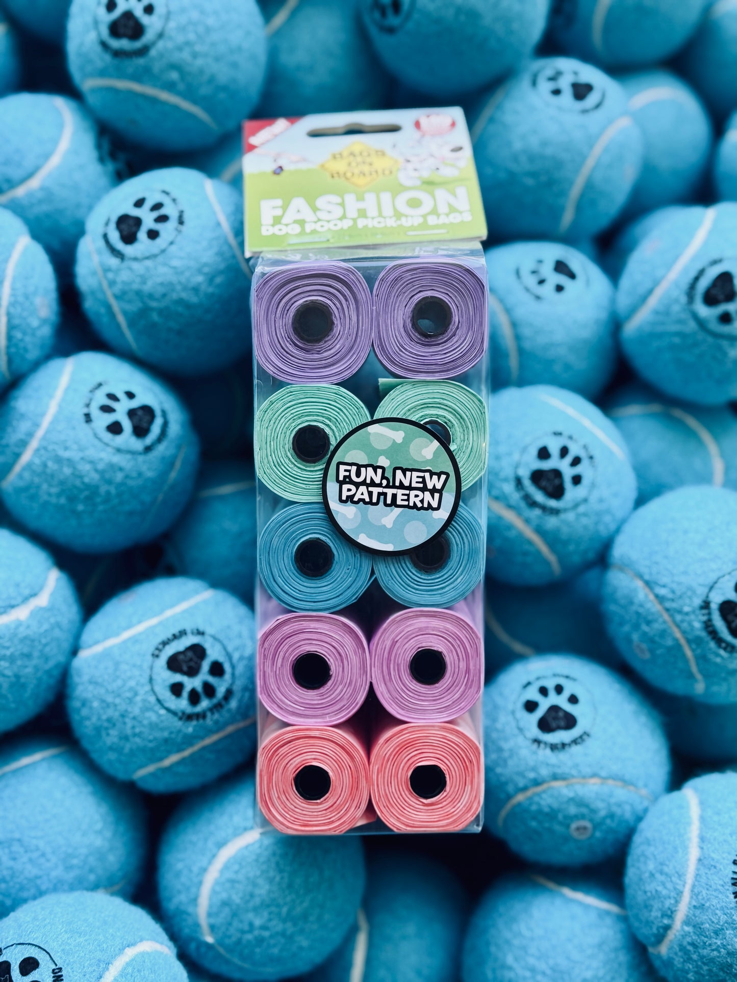A pack of multicolored dog waste bags with a pattern, placed on a surface covered with blue tennis balls.