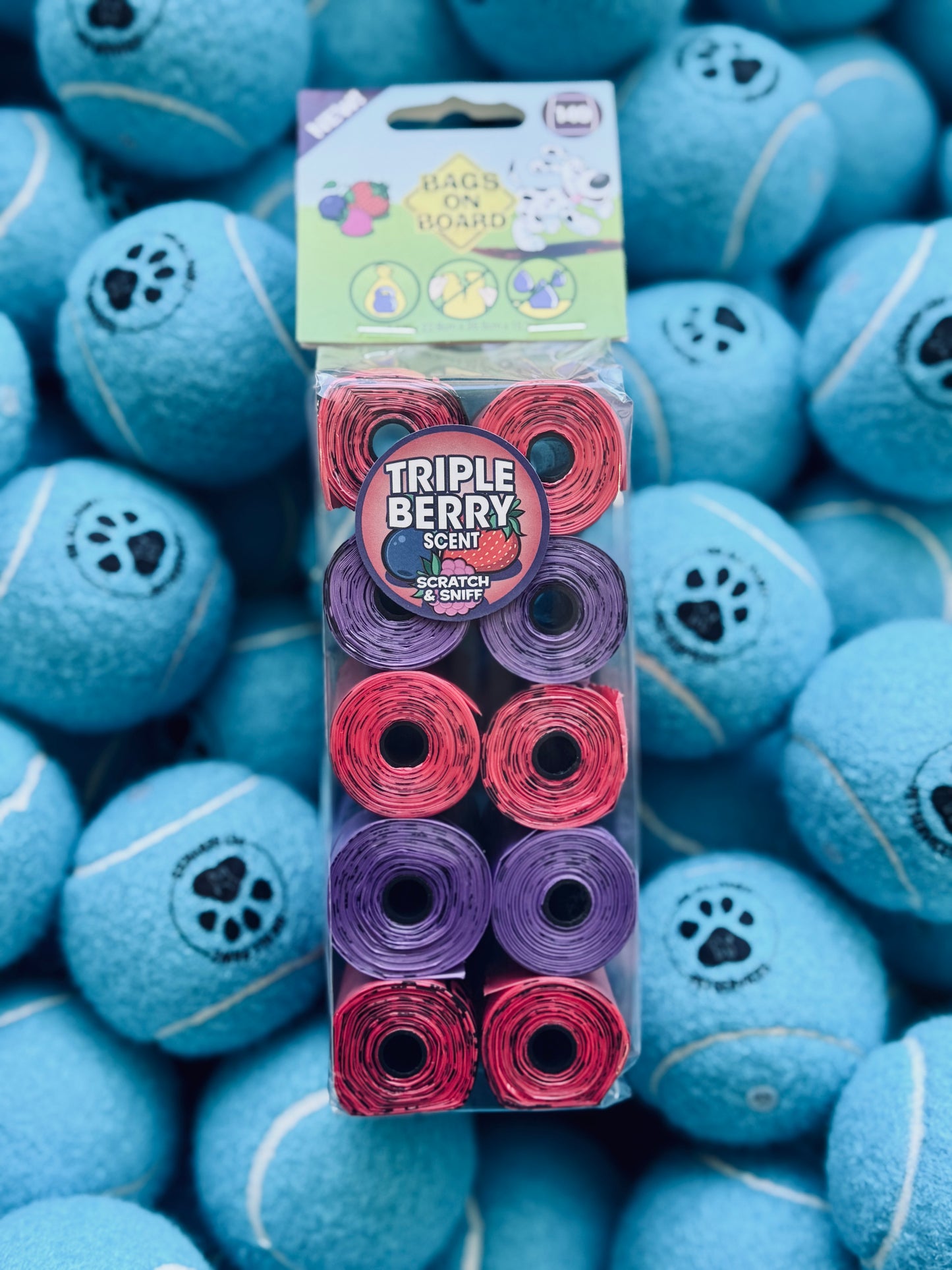 A pack of Bags On Board Berry Scented dog waste bags, displayed with blue tennis balls.