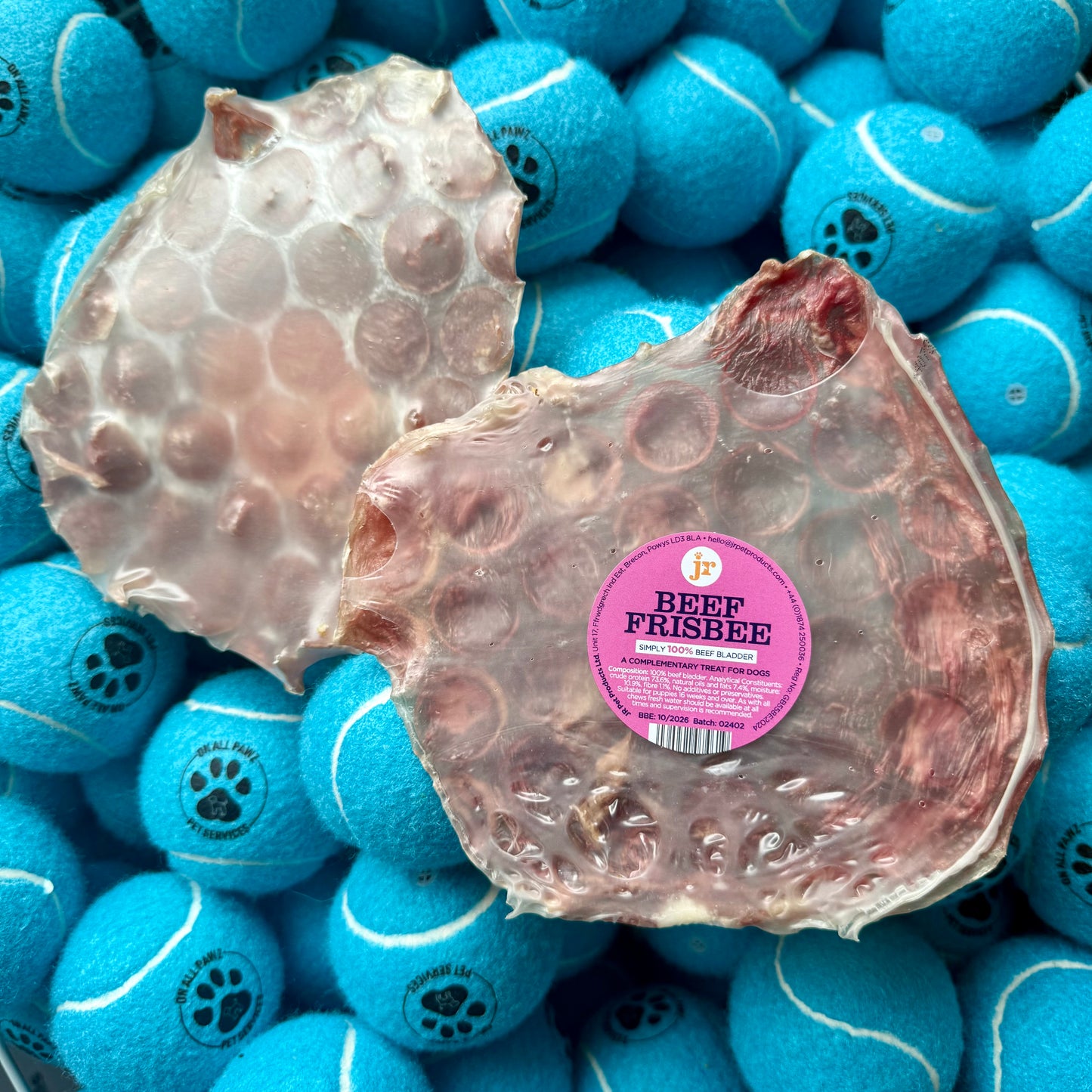 Two beef frisbees with a pink label on a bed of blue tennis balls.