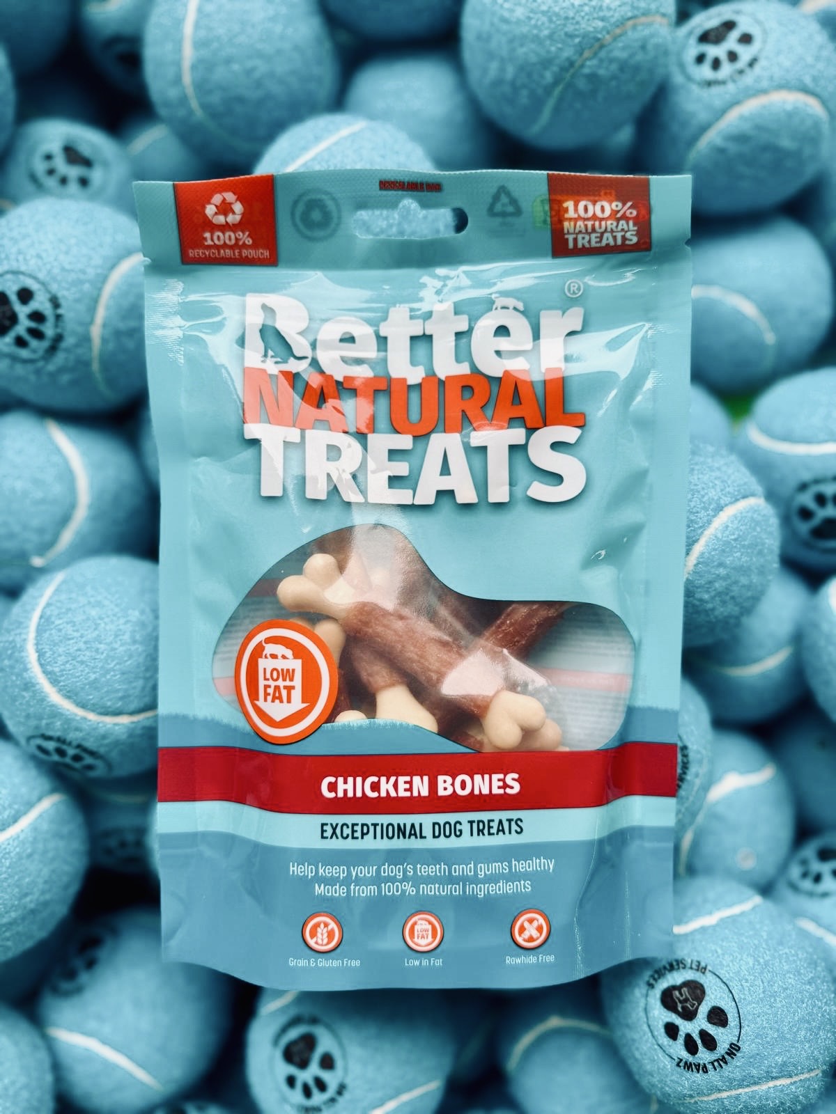 Package of 'Better Natural Treats' chicken bones dog treats surrounded by blue tennis balls.