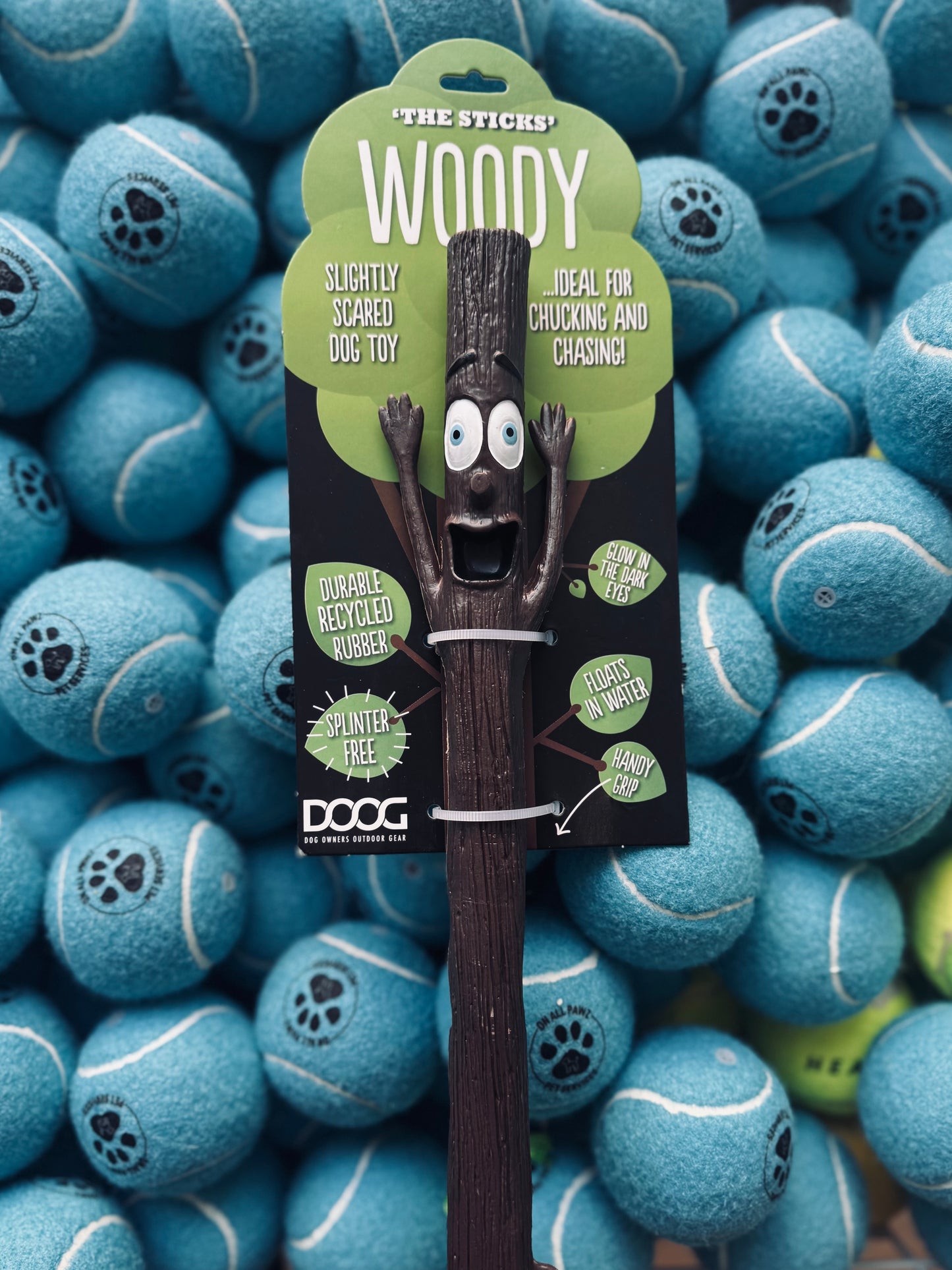 A DOOG Mr. Stick - Woody, a fetch toy for dogs, displayed in front of multiple blue tennis balls.