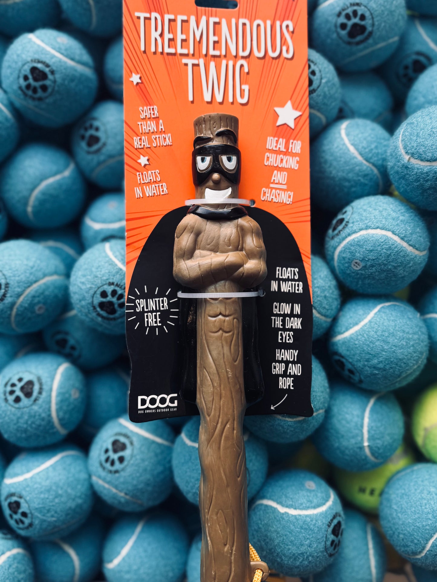 A synthetic dog toy designed to resemble a twig, with a built-in rope for throwing, displayed on a background of tennis balls.