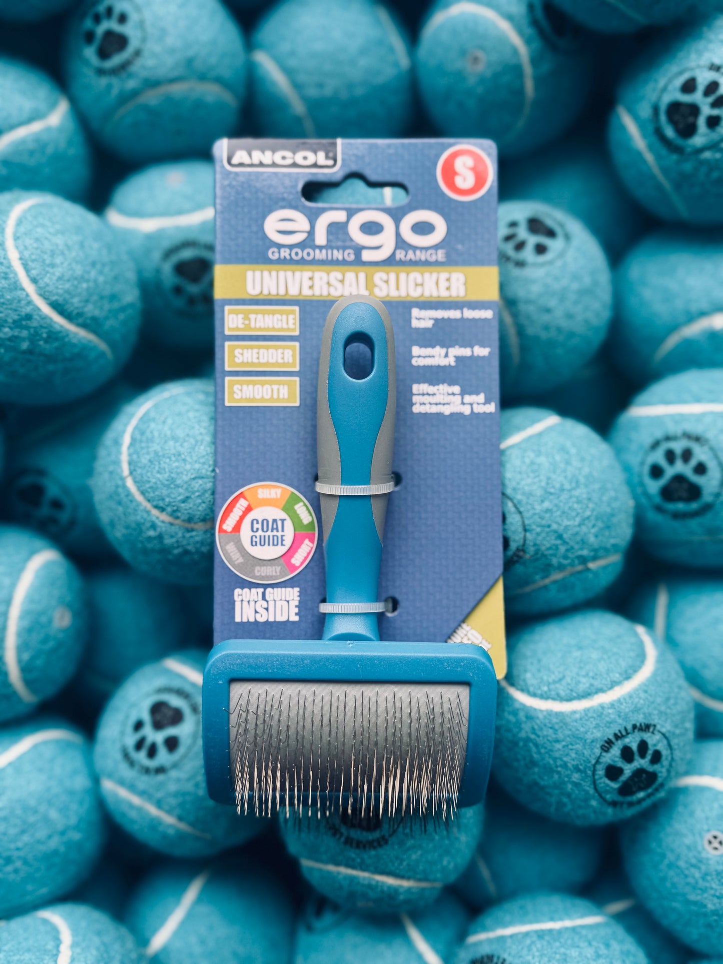 An Ancol Ergo Slicker Brush for pets displayed on a surface with blue tennis balls, indicating the small size of the brush suitable for small breeds or cats.