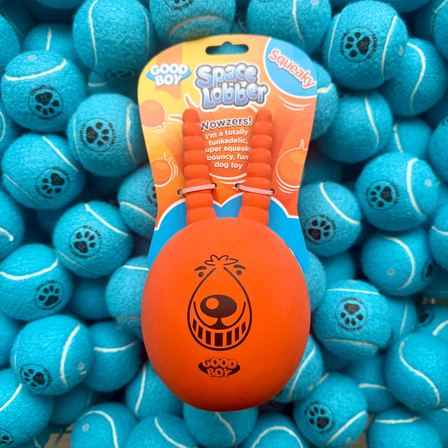 Orange Space Lobber toy with packaging on a background of blue tennis balls