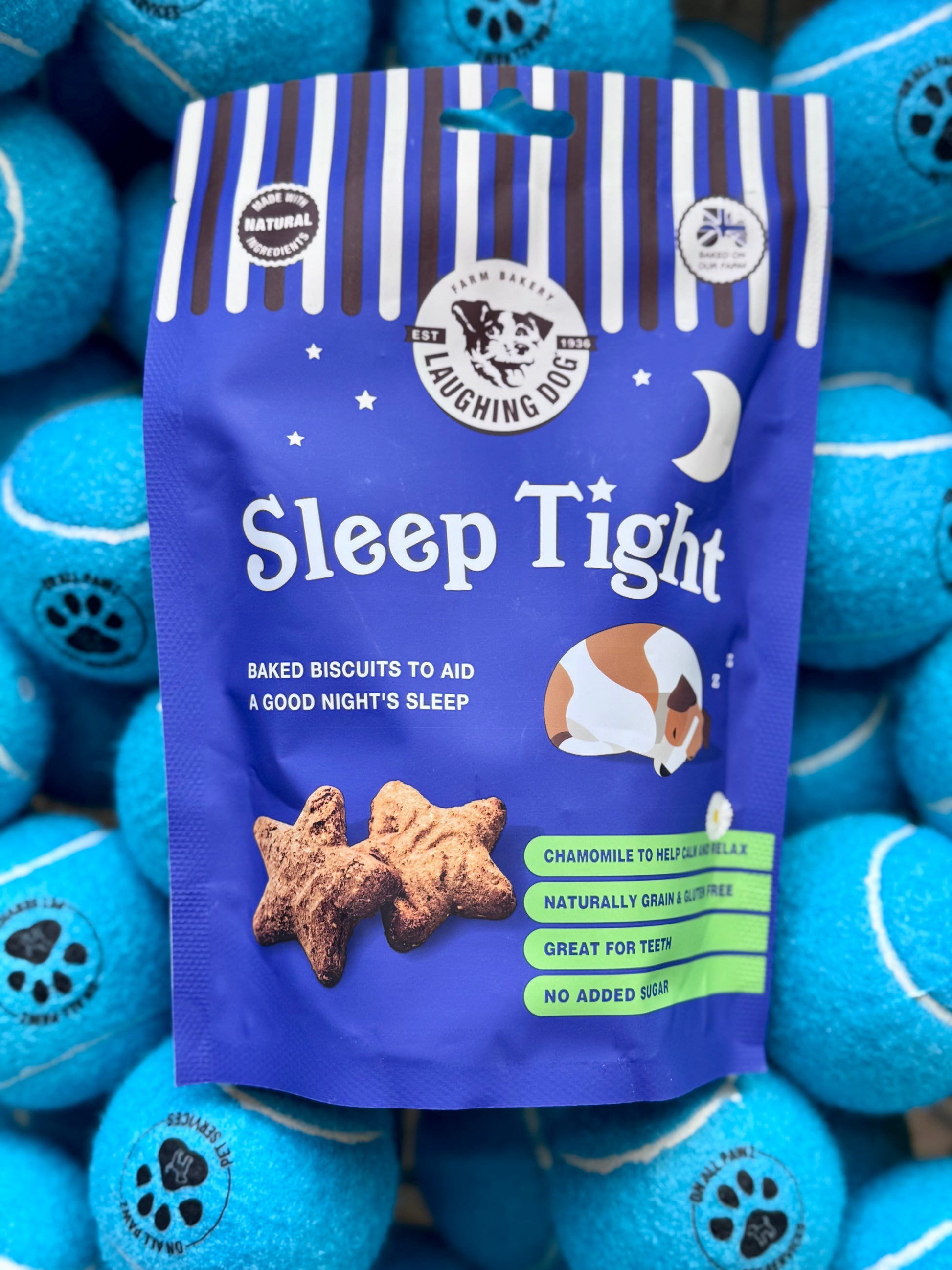 Packaging of 'Sleep Tight' grain-free dog treats with a picture of a dog and the background featuring the product name in a decorative font, alongside blue dog toys.