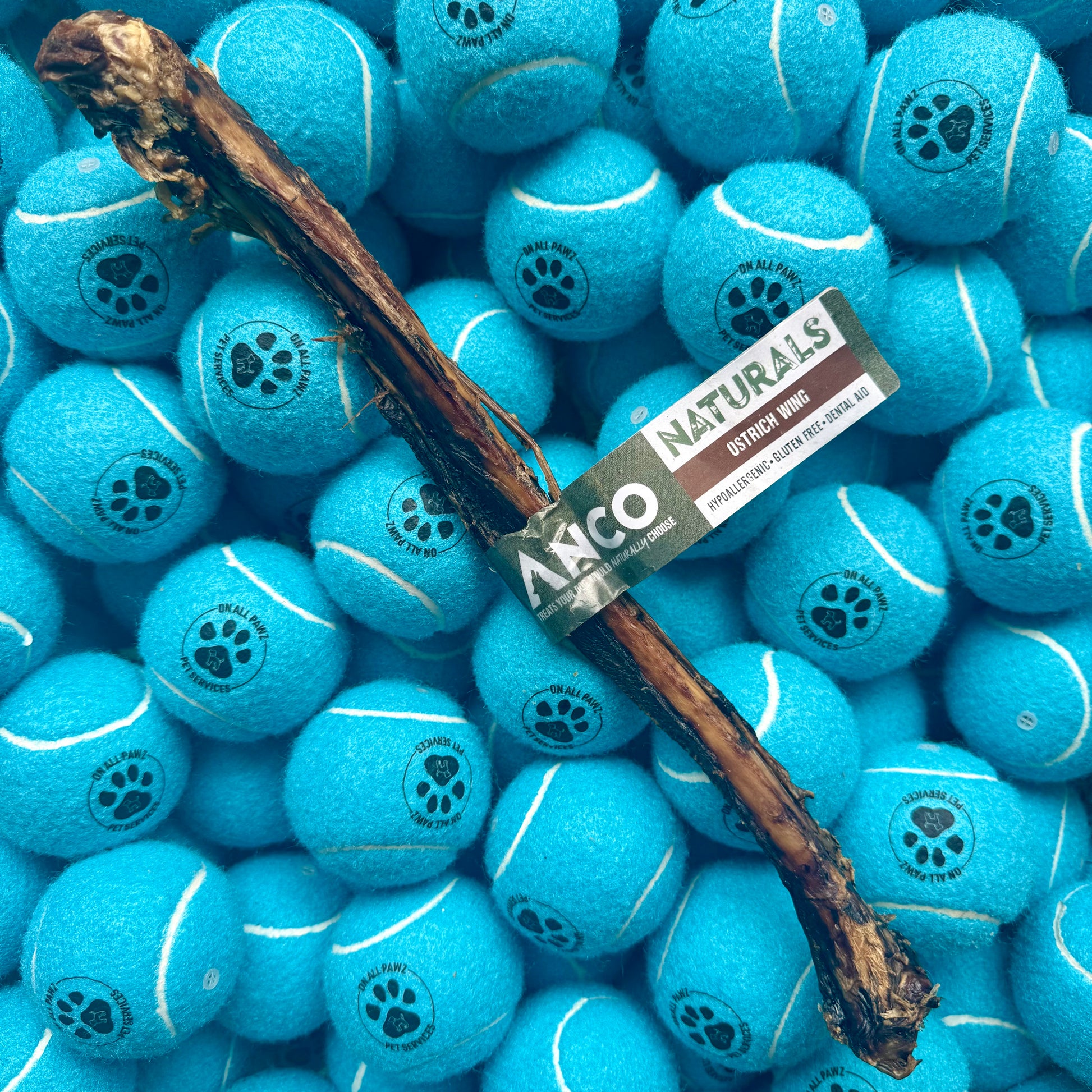 Blue tennis balls with a dog chew stick and ANCO Naturals label on a pile of balls.