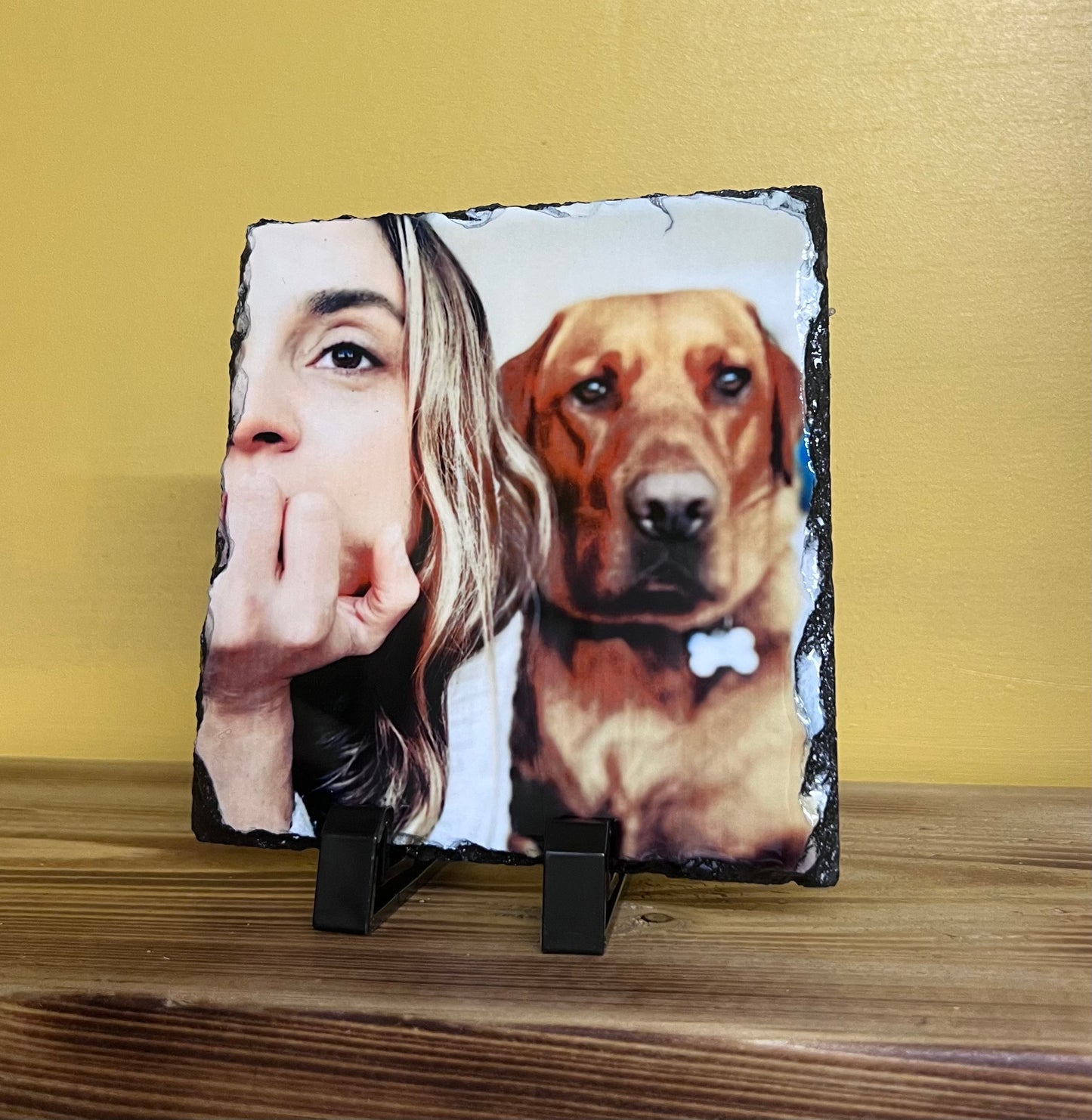 A square-shaped personalized slate plaque with an engraved image of a person and a dog on it, displayed on a wooden surface.