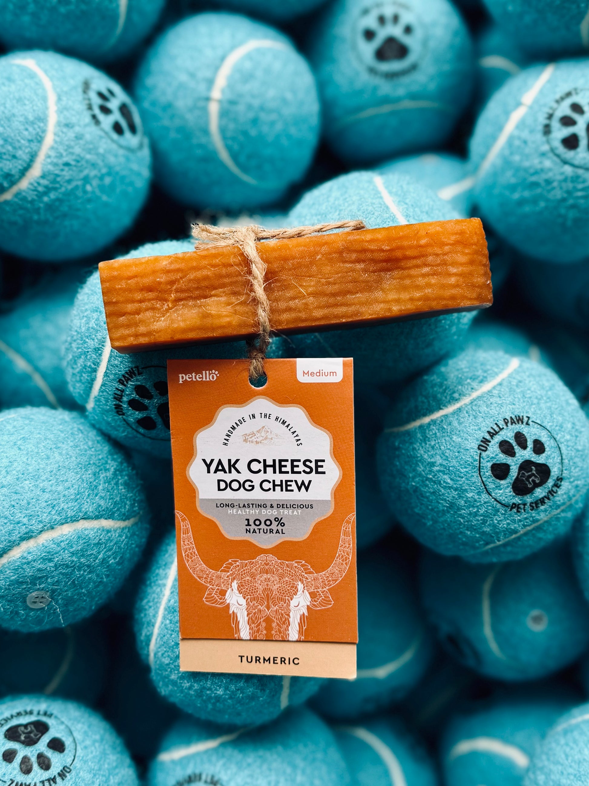 A yak cheese dog chew treat infused with turmeric, placed on a bed of blue tennis ball-shaped treats.