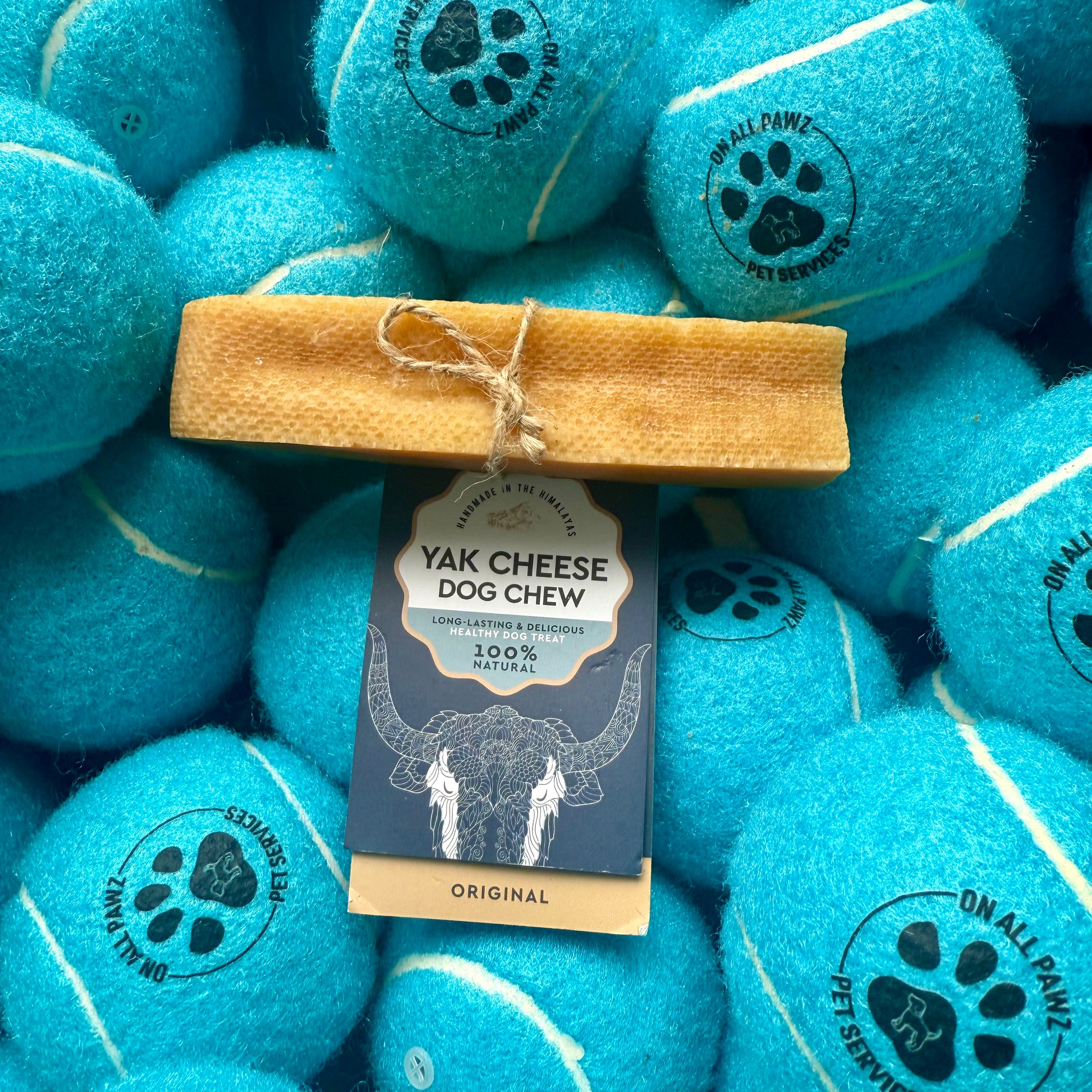 Yak cheese dog chew with a package on top of blue tennis balls.