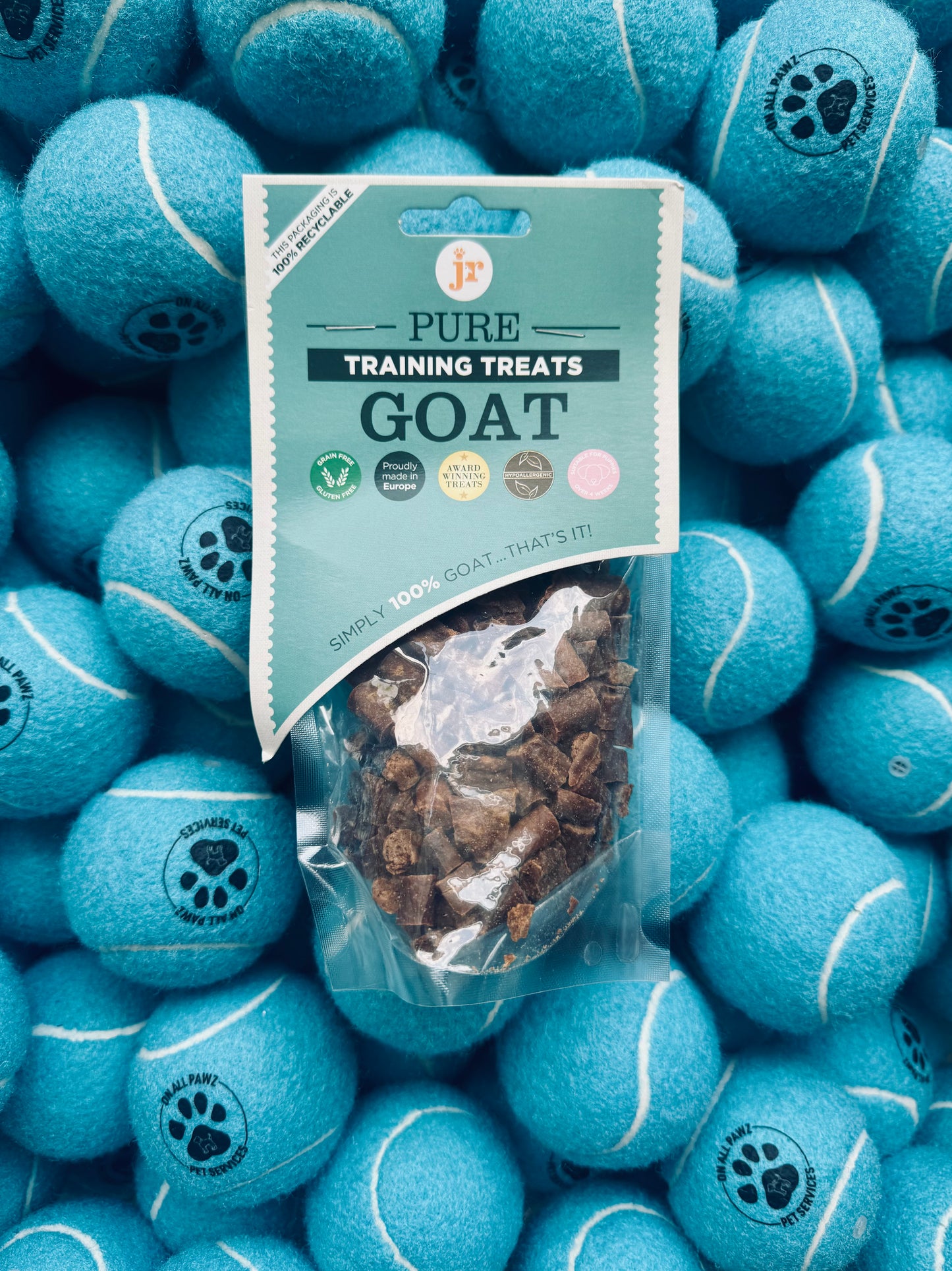 Bag of goat training treats surrounded by blue tennis balls with paw prints on a pile.