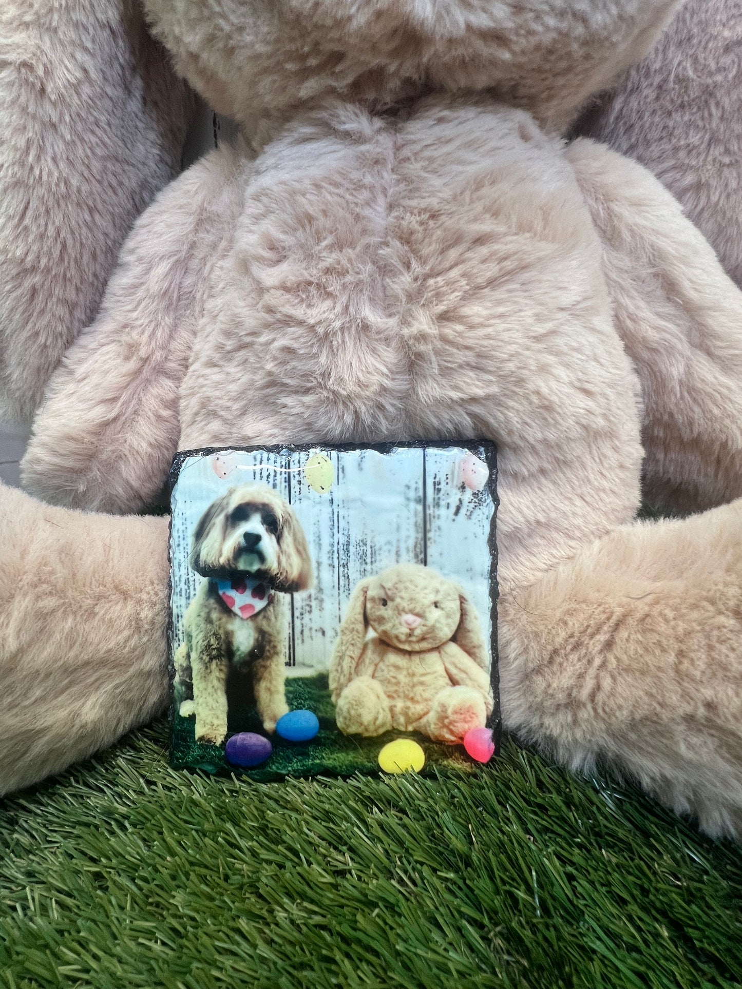 A personalized square coaster with a photo of a dog printed on it, placed on a brown fuzzy surface, likely a pet bed.