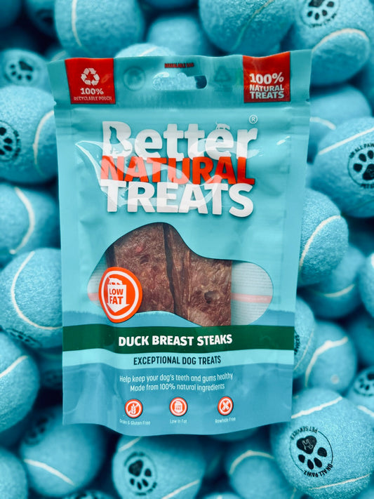 Packaging of Better Natural Treats duck breast steaks dog treats surrounded by blue tennis balls.