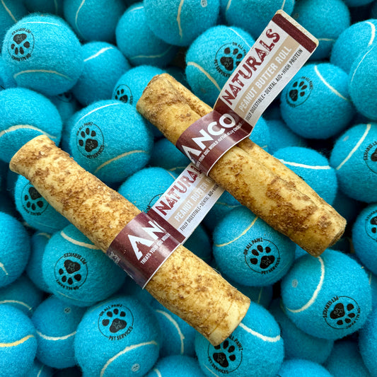 Two ANCO Naturals dog treats on a bed of blue tennis balls with paw prints.