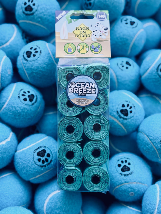 A pack of Bags On Board Ocean Breeze scented dog waste bags, with the product visible against a background of blue dog treats shaped like tennis balls.