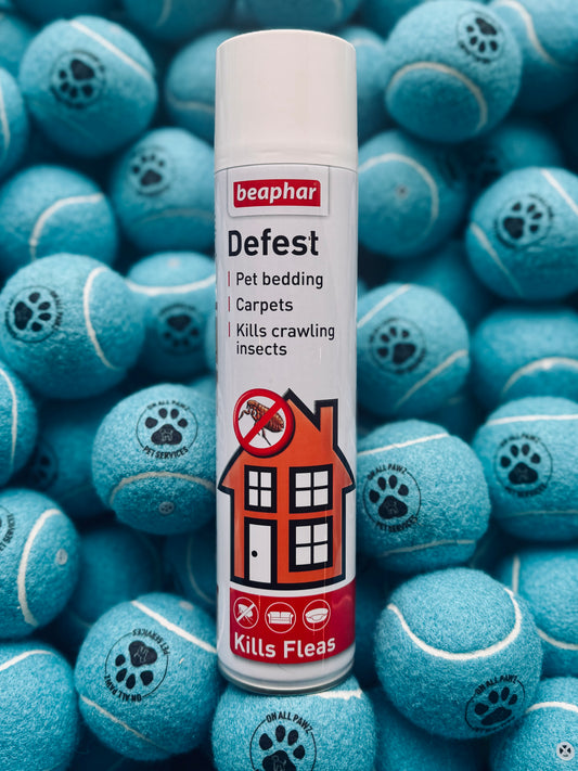 A bottle of Beaphar Defest pet room spray, designed to kill fleas and ticks, with a background of blue tennis balls each decorated with a paw print.