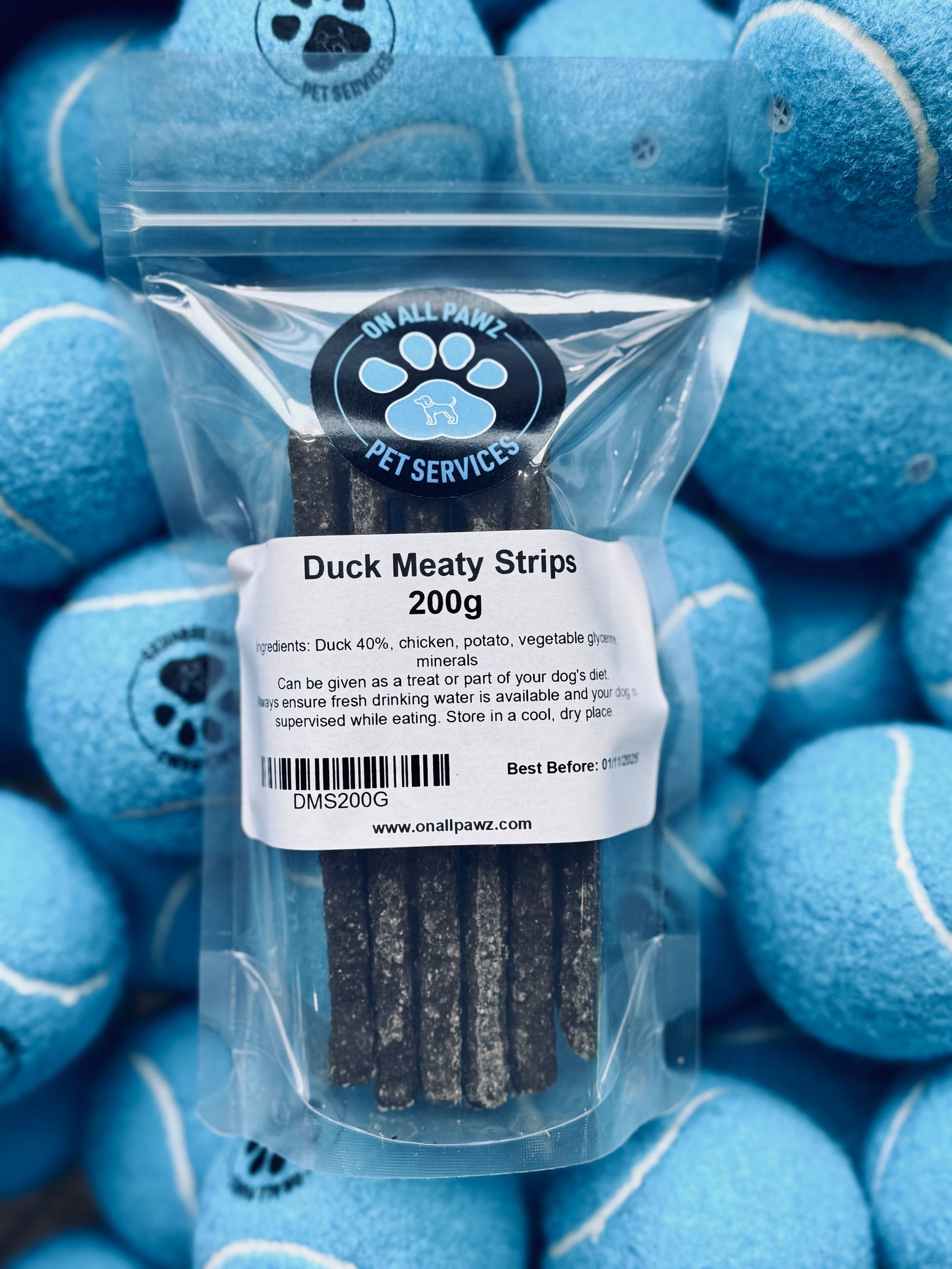 Packaging of Duck Meaty Strips dog treats, showing the product name and weight, against a background of blue dog toys.