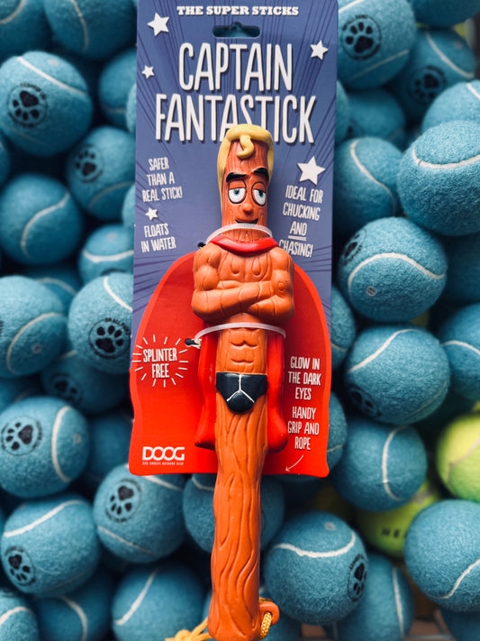 A red and orange dog toy designed to look like a stick with a cartoon character's face on it, displayed in front of a background of tennis balls.