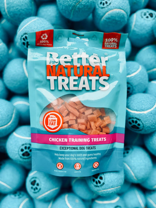 Package of 'Better Natural Treats' chicken training treats surrounded by blue tennis balls.
