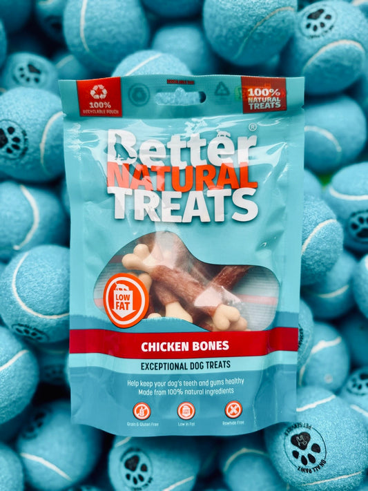 Package of 'Better Natural Treats' chicken bones dog treats surrounded by blue tennis balls.