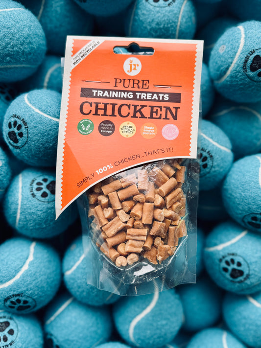 A package of JR Pure Chicken Training Treats placed on a surface with blue dog toys shaped like tennis balls in the background.