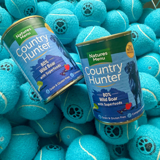 Two cans of Natures Menu Country Hunter dog food surrounded by blue tennis balls.
