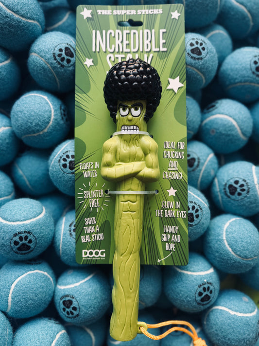 A green, cartoon-like dog toy designed to resemble a stick figure, placed on a background of blue tennis balls.