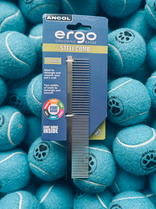A stainless steel pet comb with dual-length teeth, presented in packaging that reads 'ergo STEEL COMB'. The comb is displayed against a background of blue tennis balls.