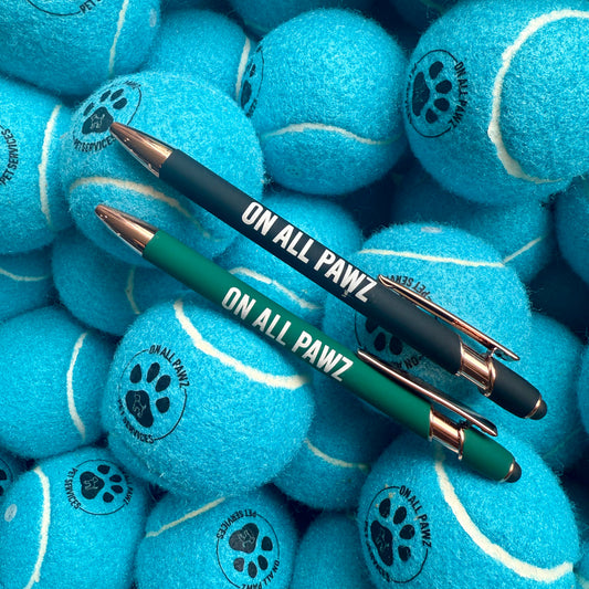Two pens with 'ON ALL PAWZ' branding on a pile of blue tennis balls.