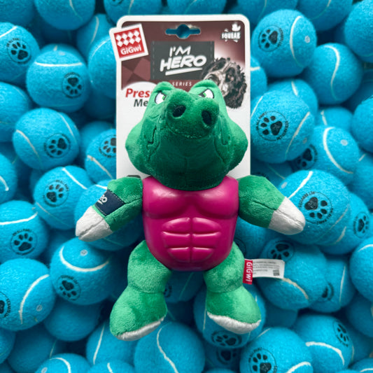 Green plush toy with a pink chest on a blue tennis ball background