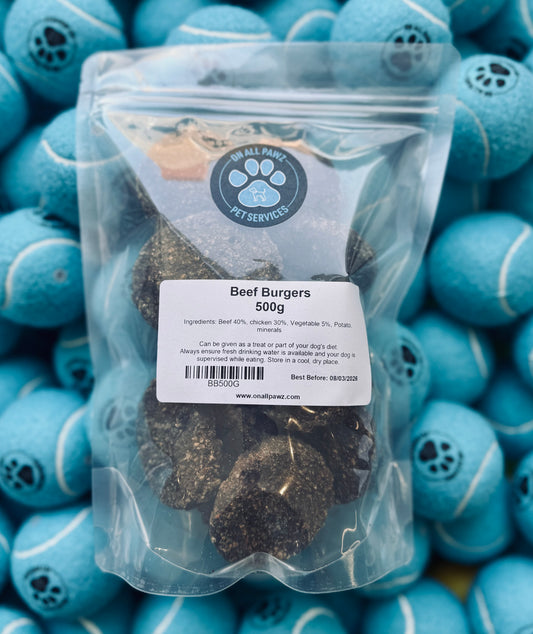 Packaged gourmet beef burgers in a clear plastic bag, with product labeling visible, placed against a background of blue pet toys.