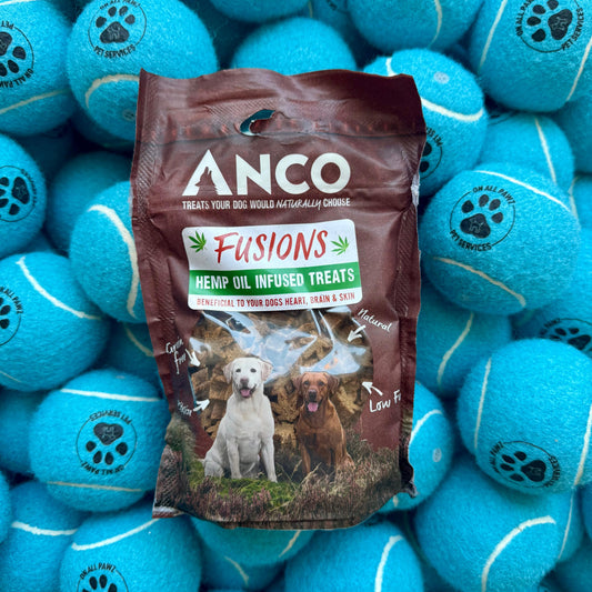 Anco Fusions Hemp Oil Infused Treats package surrounded by blue tennis balls with paw prints.