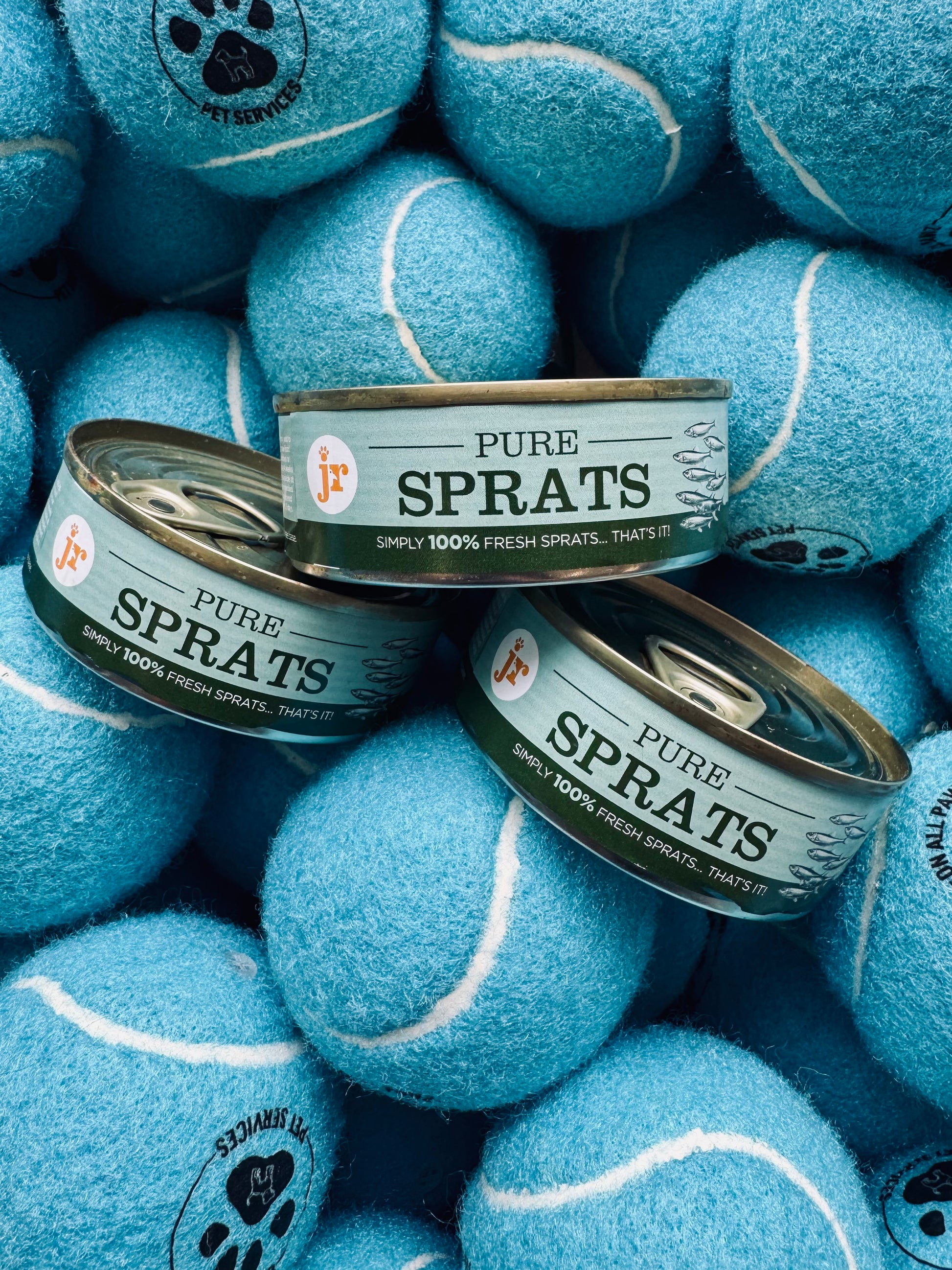 Cans of 'Pure Sprats' surrounded by blue tennis balls with paw prints.