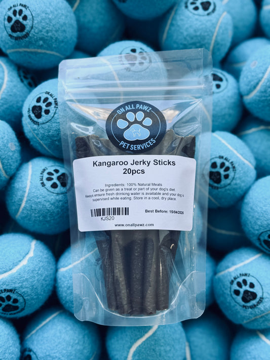 A clear plastic packaging containing Kangaroo Jerky Sticks with a label showing the product name and a paw print design. The packaging is displayed atop a collection of blue tennis balls with a paw print design.
