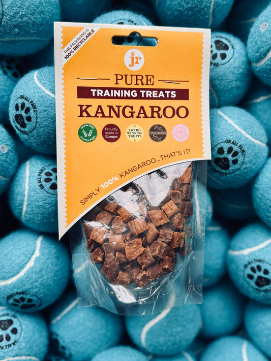A package of Pure Kangaroo Training Treats is displayed with visible treat pieces, against a background of blue dog toys.