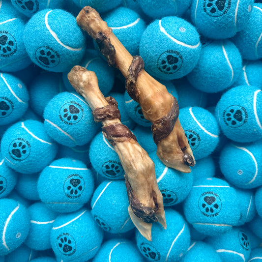Two dog bones on a bed of blue tennis balls with paw prints.