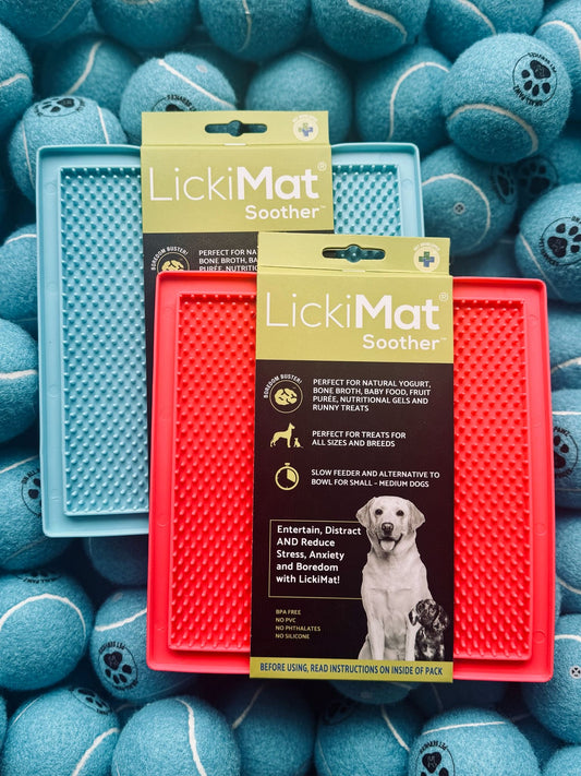 Two LickiMat Soothers, one red and one blue, on a background of blue tennis balls.