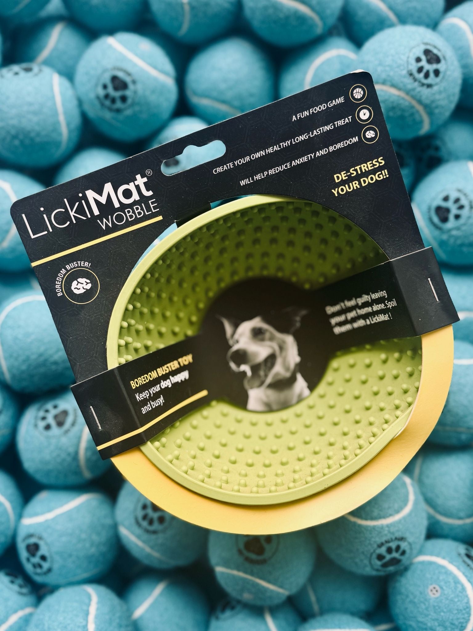 Green LickiMat Wobble toy in packaging surrounded by blue tennis balls