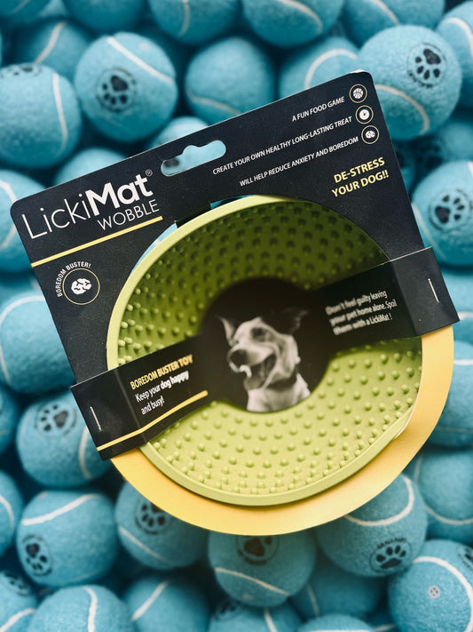Green LickiMat Wobble toy in packaging surrounded by blue tennis balls