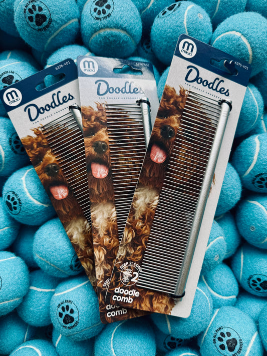 Three dog grooming combs in packaging surrounded by blue tennis balls with paw prints.