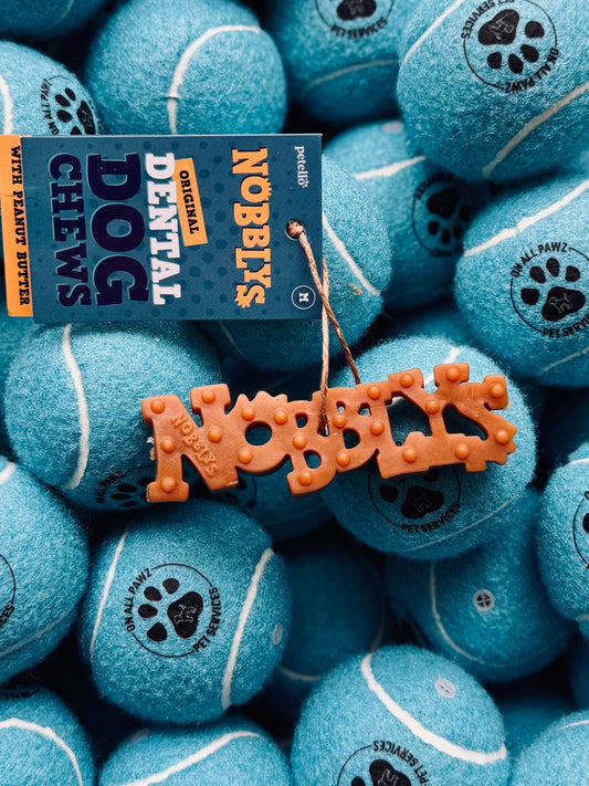 A close-up of a dog chew toy with the text 'NOBBLYS' on it, surrounded by multiple tennis ball-shaped toys painted in blue.