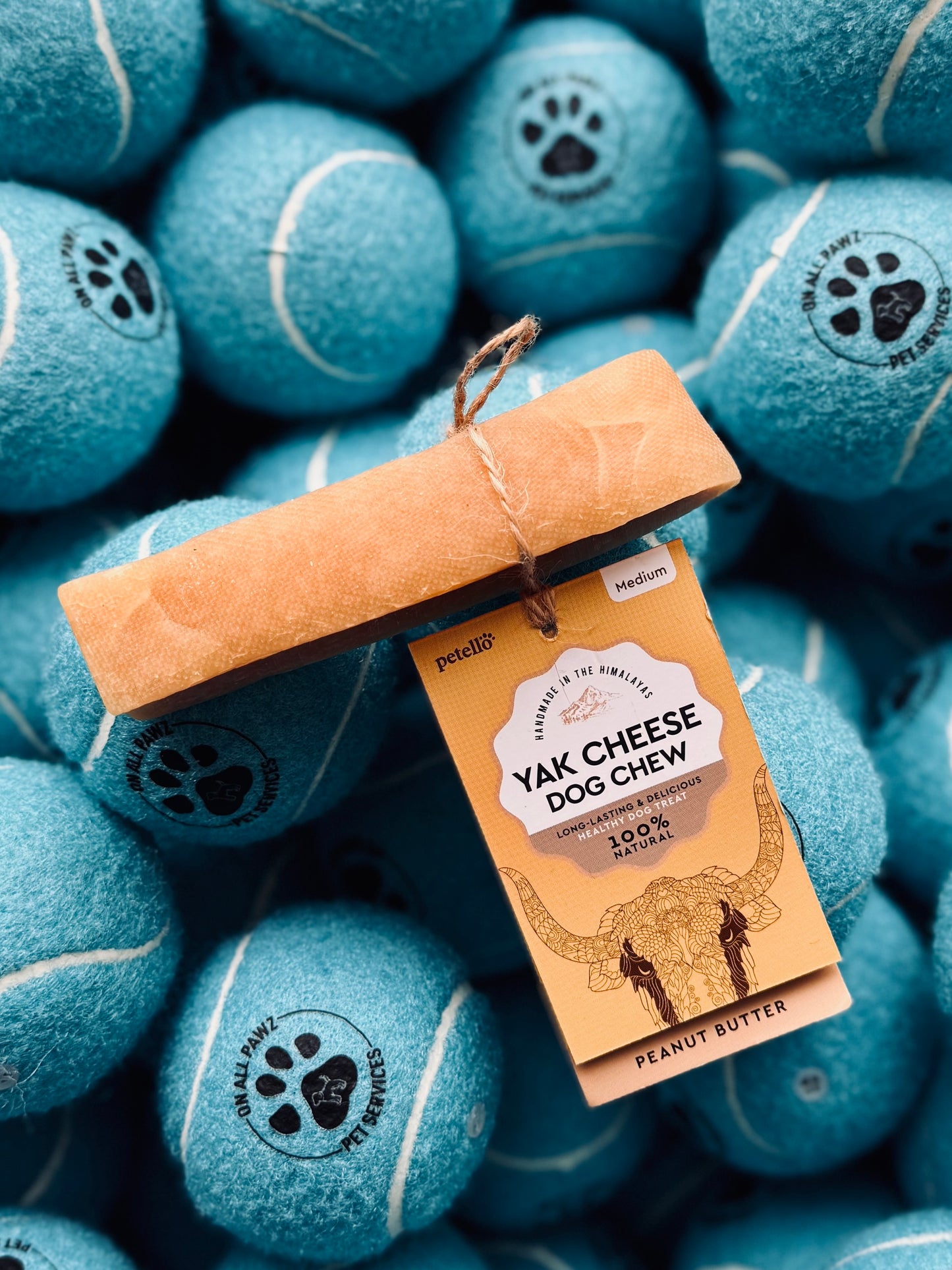 A Petello Yak Cheese Dog Chew in Peanut Butter Flavor placed on top of several tennis balls, with a tag showing the product name and brand.