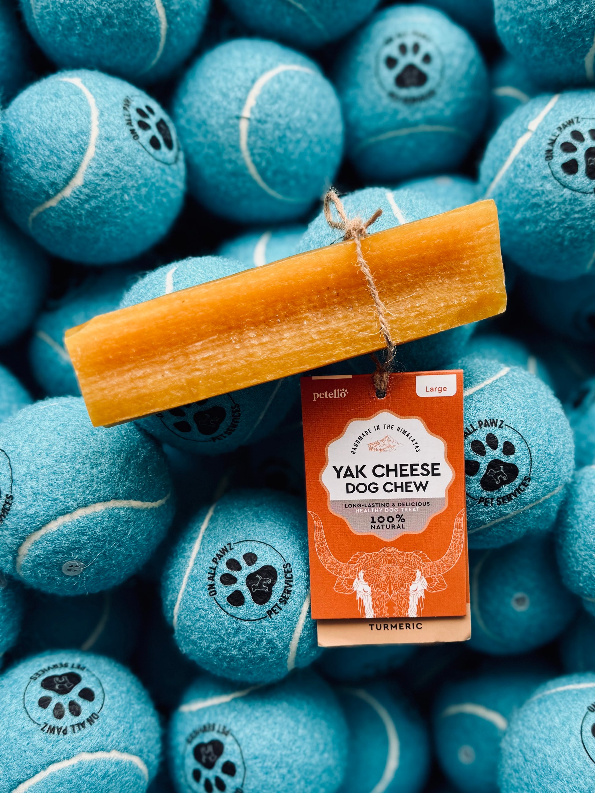 A yak cheese dog chew treat with turmeric, placed on a pile of blue tennis balls, with packaging visible showing the product and brand name.