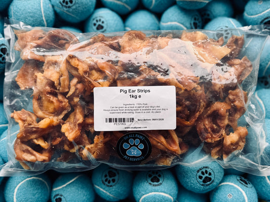 A clear plastic package containing pig ear strips, with a label showing the product name and brand. The package is placed on a surface with blue objects in the background.