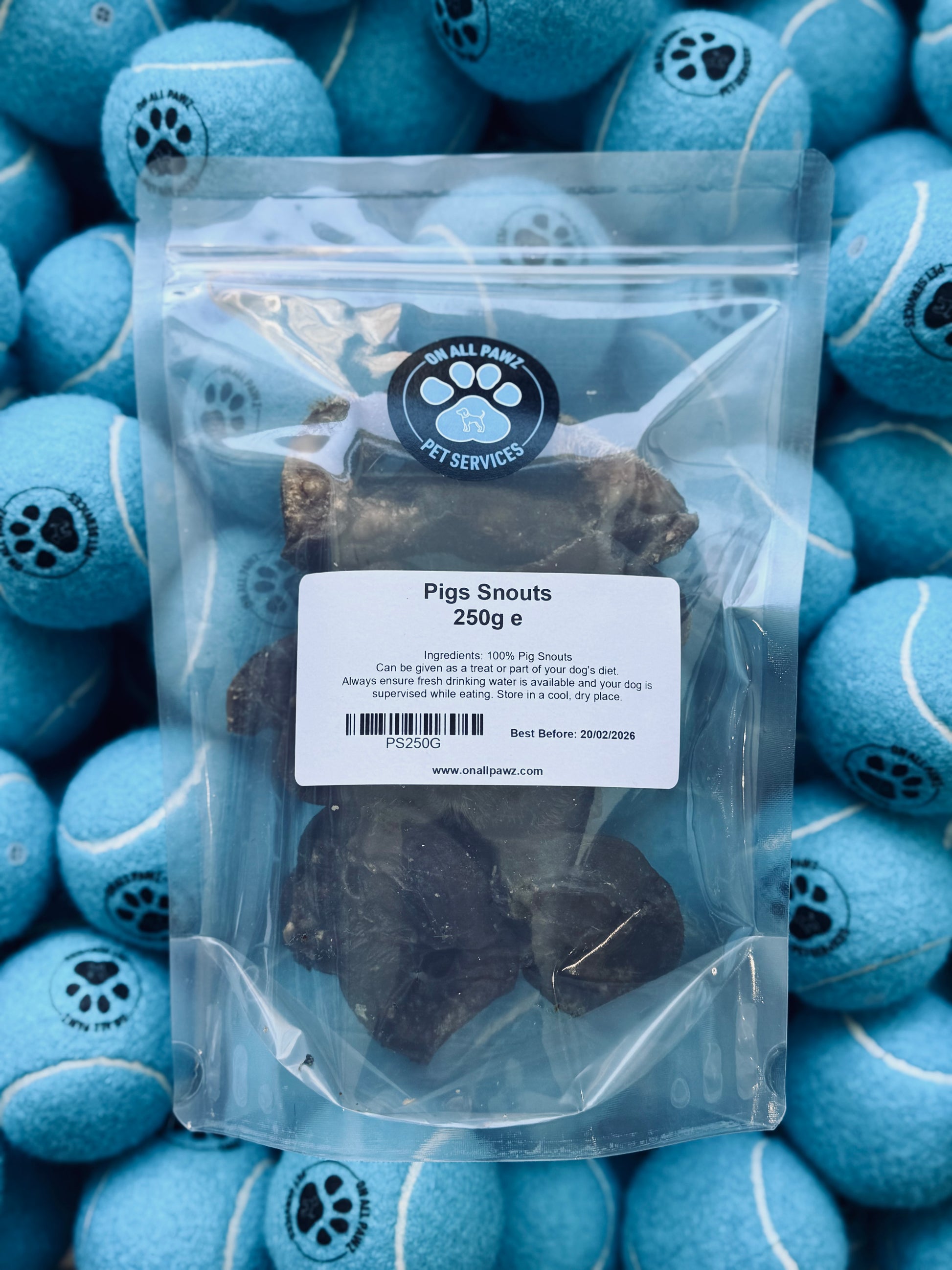 Packaged pig snouts in a clear plastic bag, with a label showing the product name and brand, placed against a background of blue tennis balls.