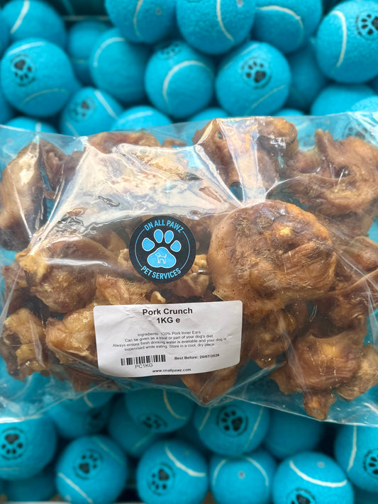 A 1KG bulk pack of natural dog treats, labeled Pork Crunch, with a visible brand logo on the label, placed on a background with blue dog toys.