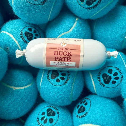 Bag of Pure Duck Pate on a pile of blue tennis balls with pet service branding.