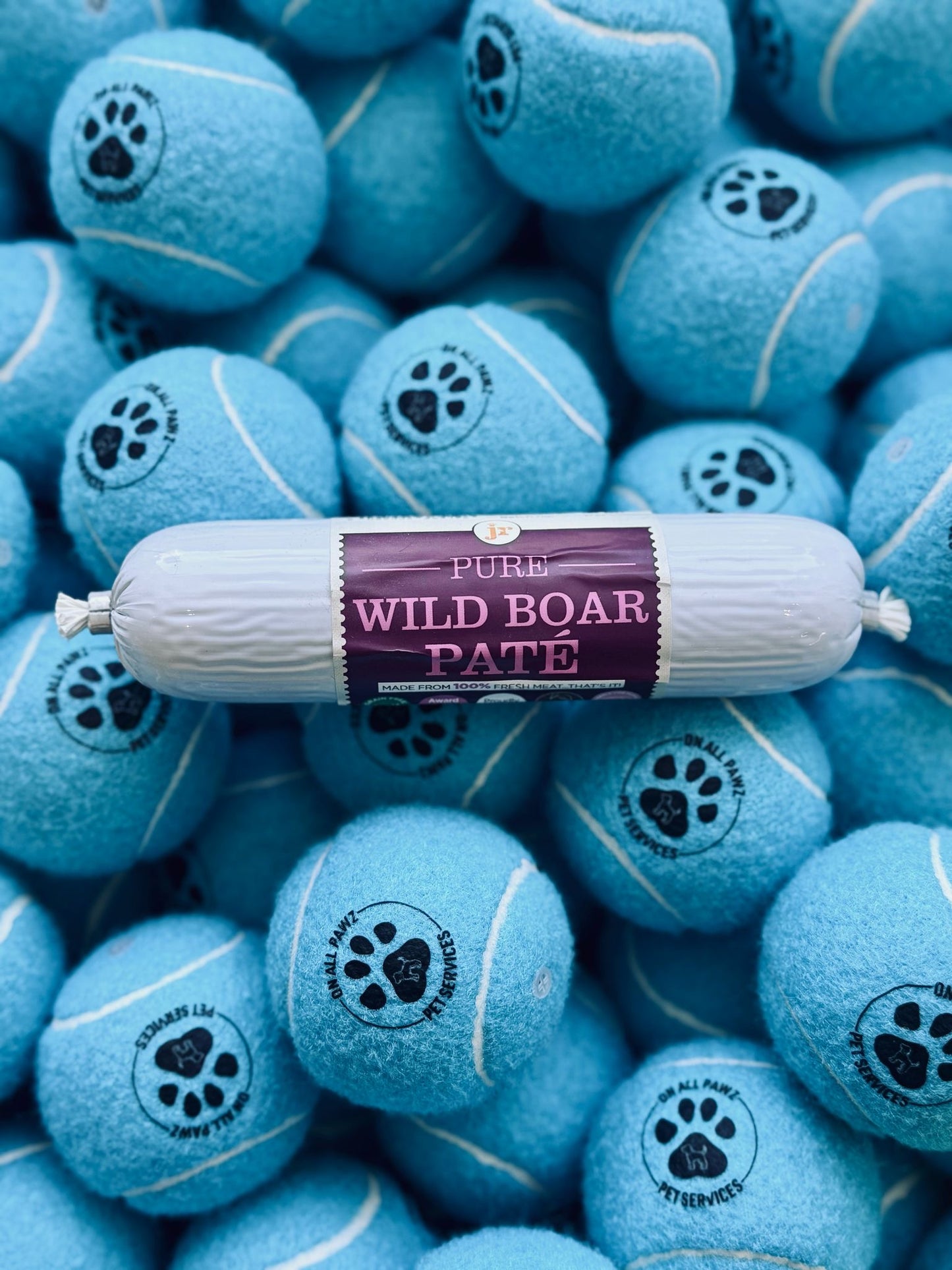 Blue tennis balls with paw prints and a roll of 'Pure Wild Boar Paste' on top.