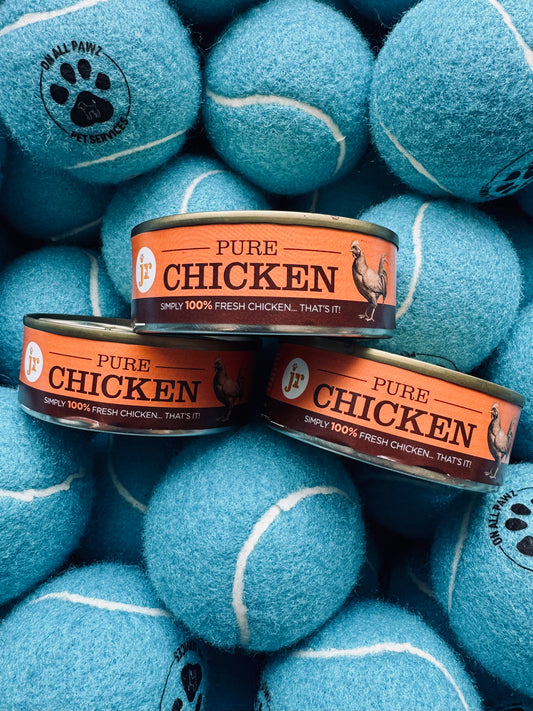 Cans of Pure Chicken pet food surrounded by blue tennis balls with paw prints.