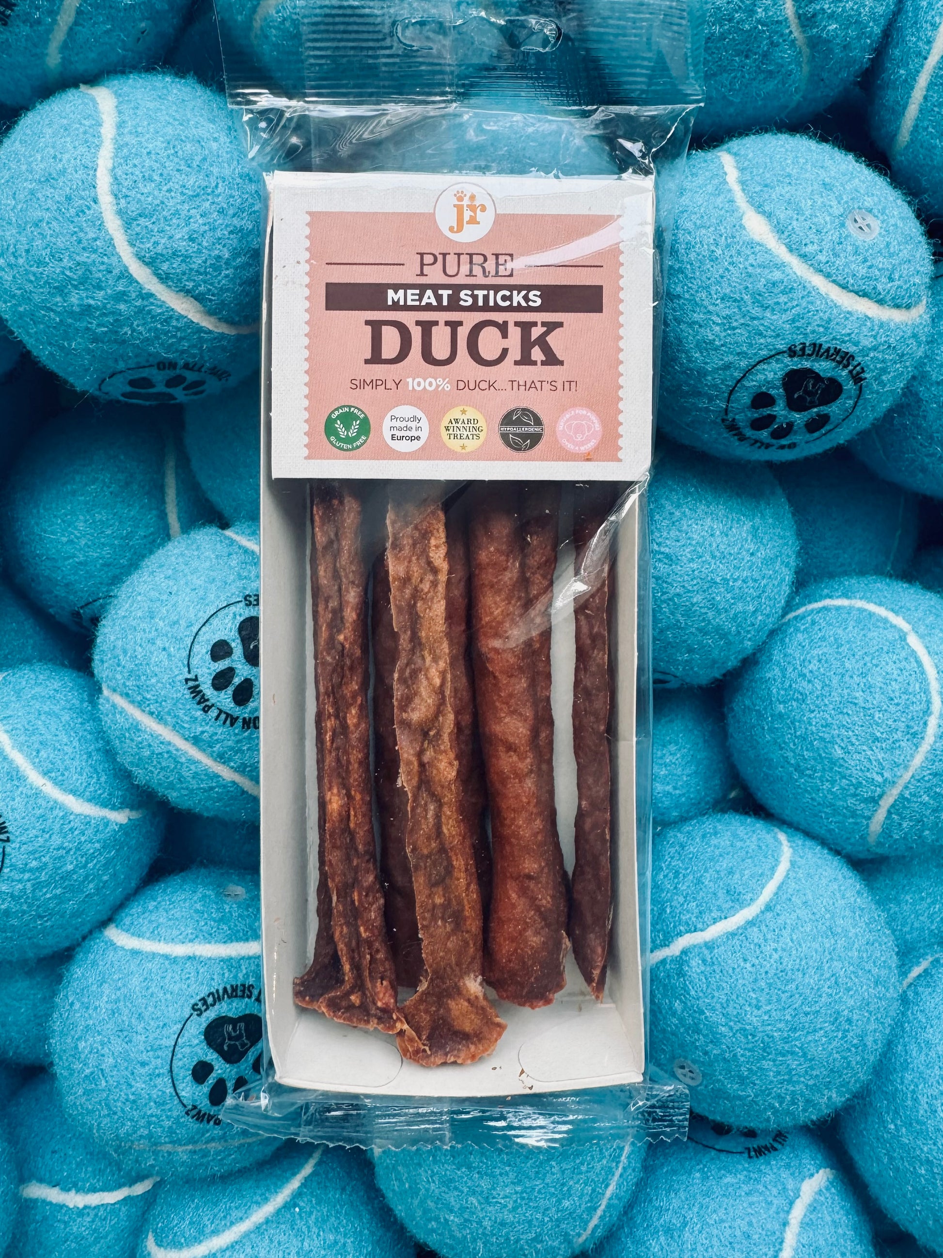 Pack of duck meat sticks with packaging on a background of blue tennis balls.